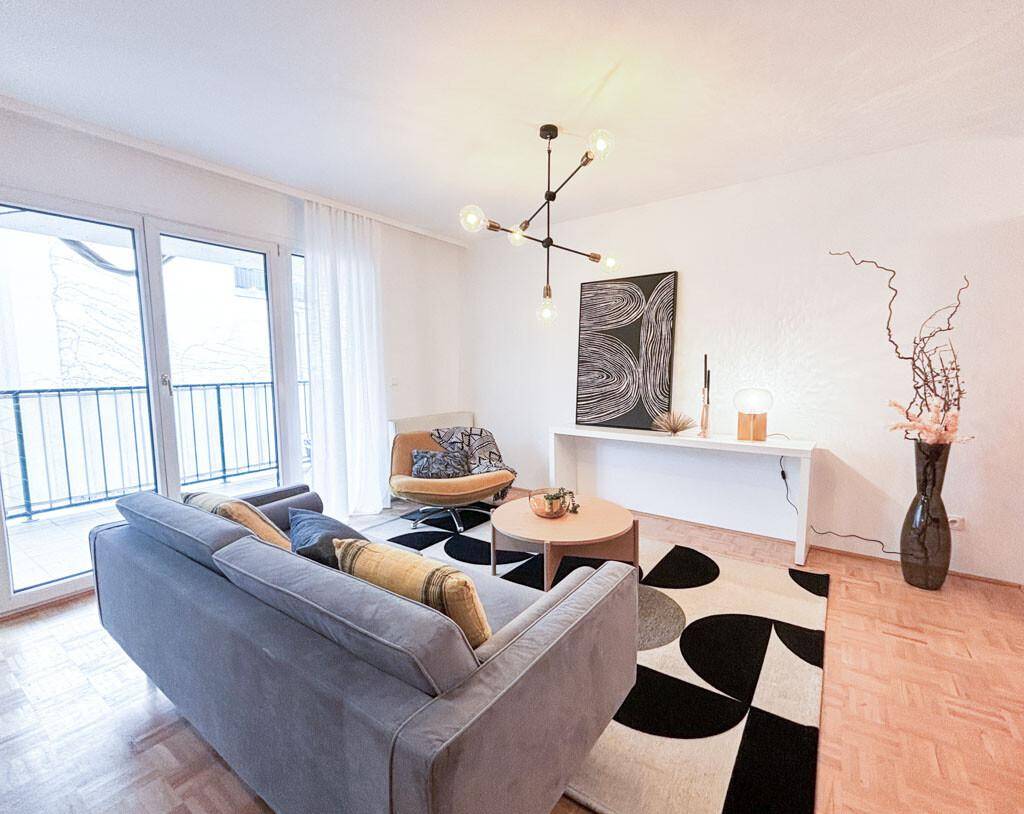 Helles Wohnzimmer mit modernem Teppich, bequemer Couch und Zugang zum Balkon.