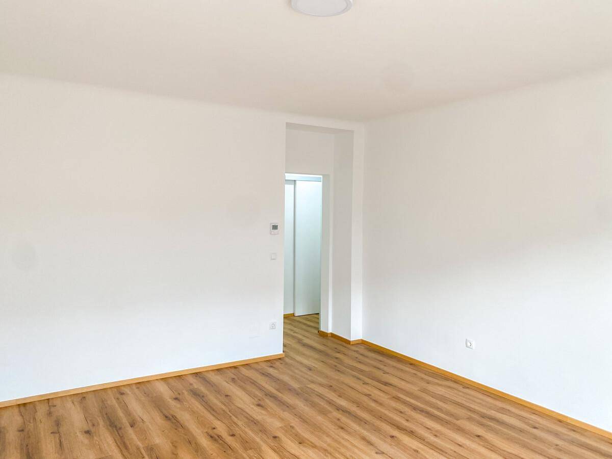 Geräumiges, leeres Zimmer mit hellem Laminatboden und frisch gestrichenen weißen Wänden.