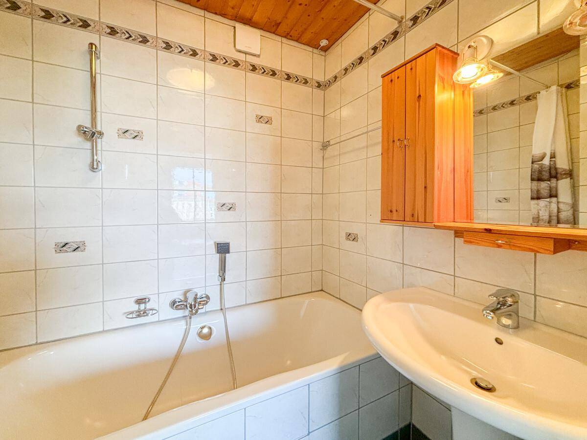 Badezimmer mit Badewanne, Waschbecken, weißen Fliesen und Holzdecke.