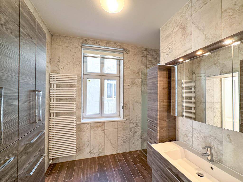 Modernes Badezimmer mit großformatigen Fliesen, Einzelwaschbecken und beheiztem Handtuchhalter.