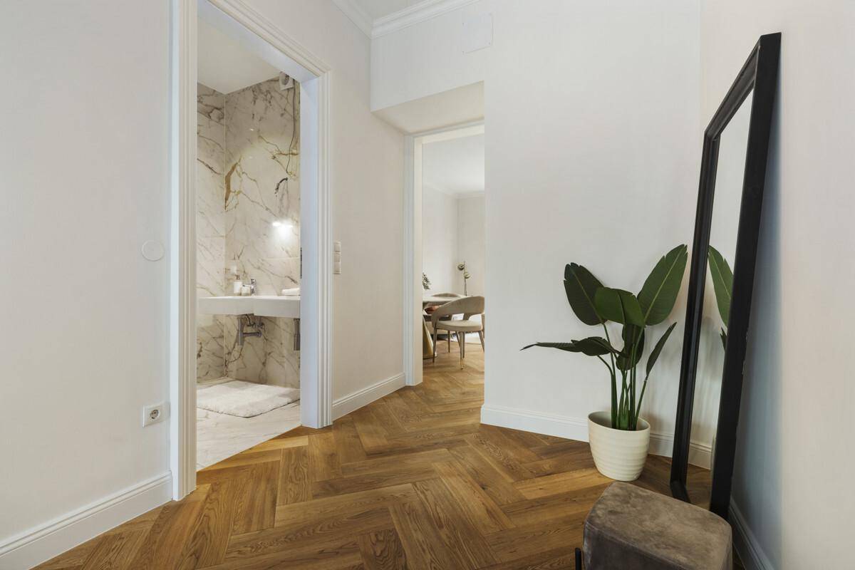 Eleganter Flur mit Fischgrätparkett und Zugang zu einem modernen Badezimmer mit Marmorfliesen.
