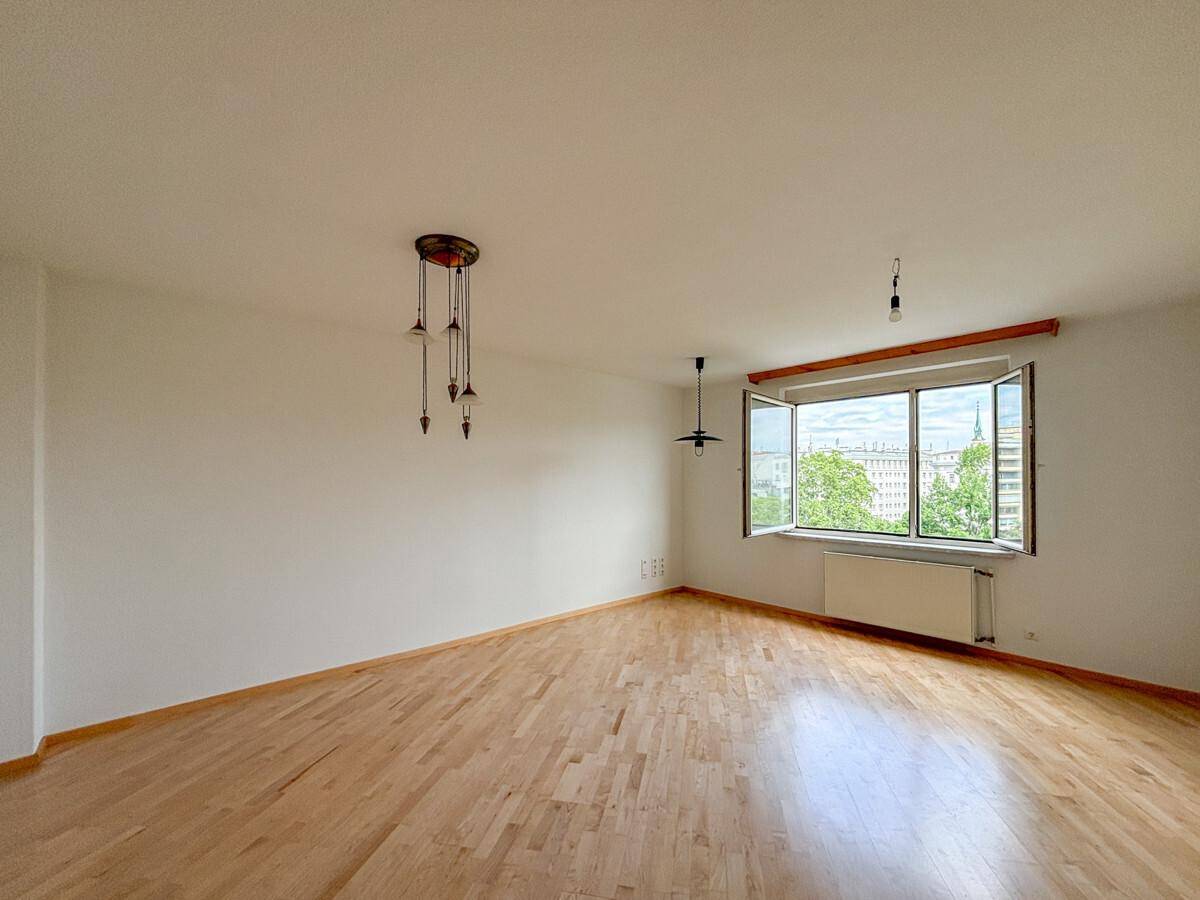 Helles, leeres Zimmer mit Holzboden und einem Fenster, das einen Blick ins Grüne bietet.