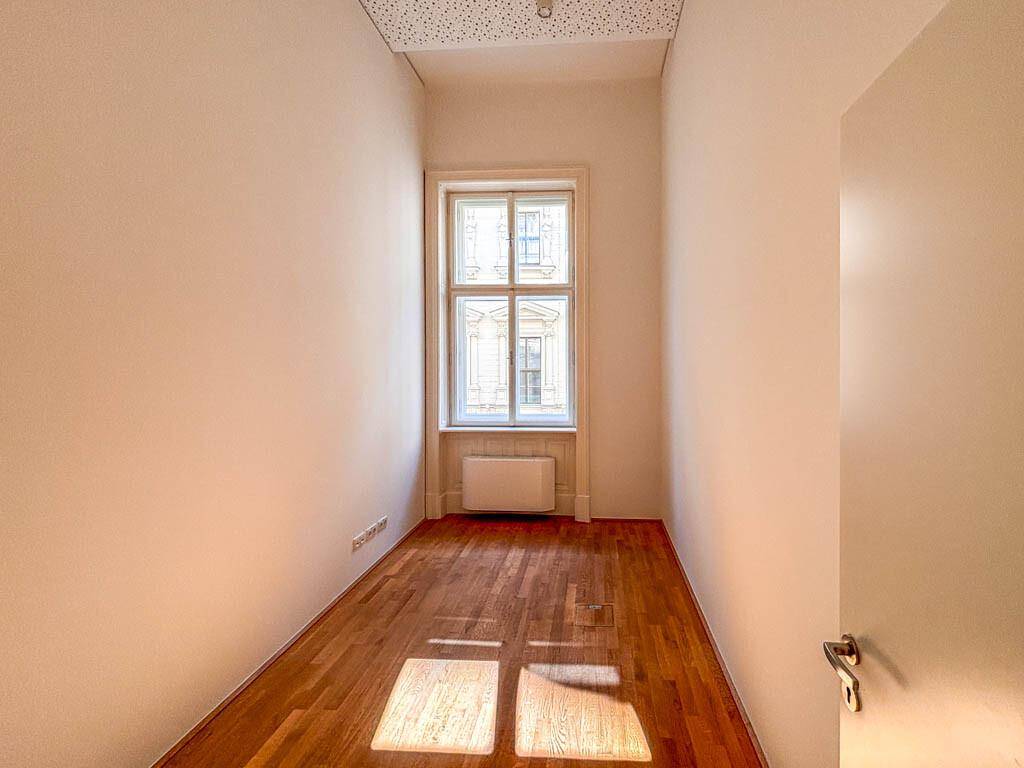 Kleiner, heller Büroraum mit Holzboden und einem großen Fenster, das viel Tageslicht hereinlässt.