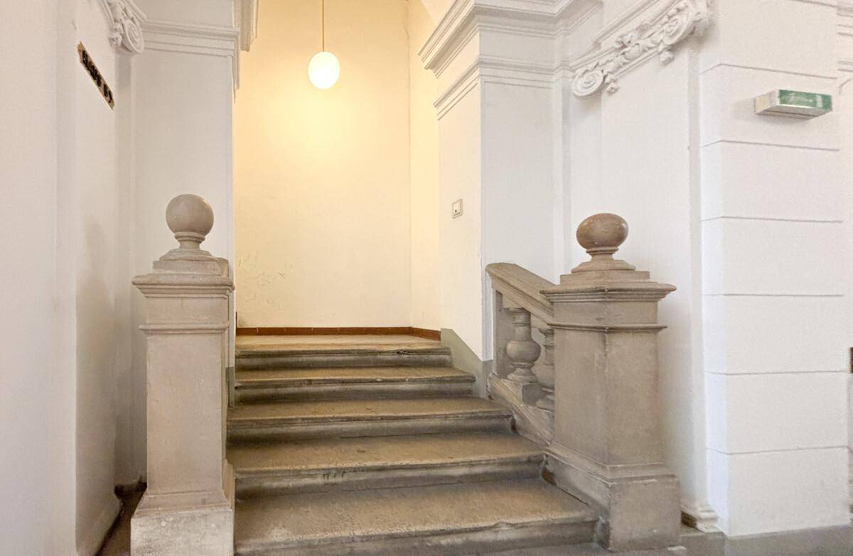 Historisches Treppenhaus mit Steinstufen und Stuckelementen, beleuchtet von einer einzelnen Deckenleuchte.