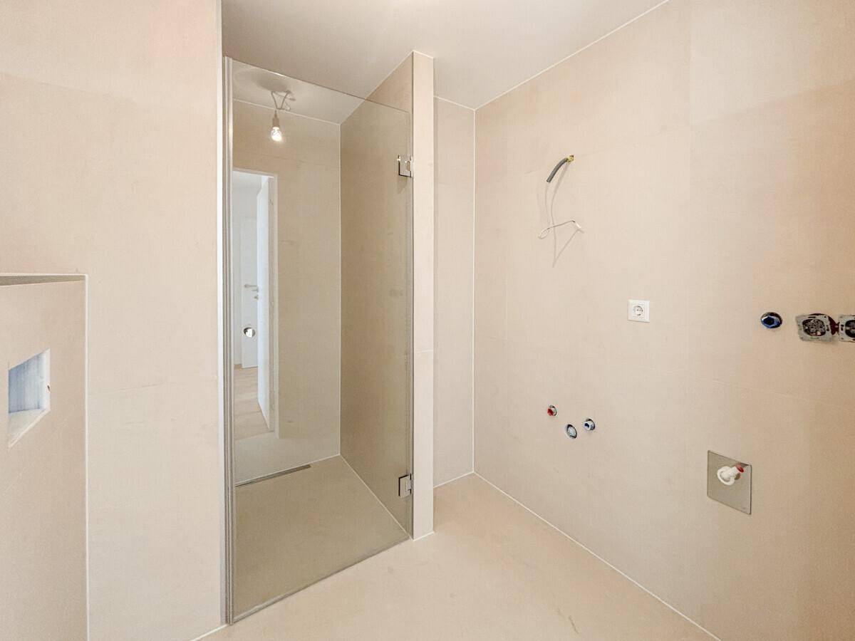Modernes Badezimmer im Rohbau mit begehbarer Dusche und hellen Fliesen.