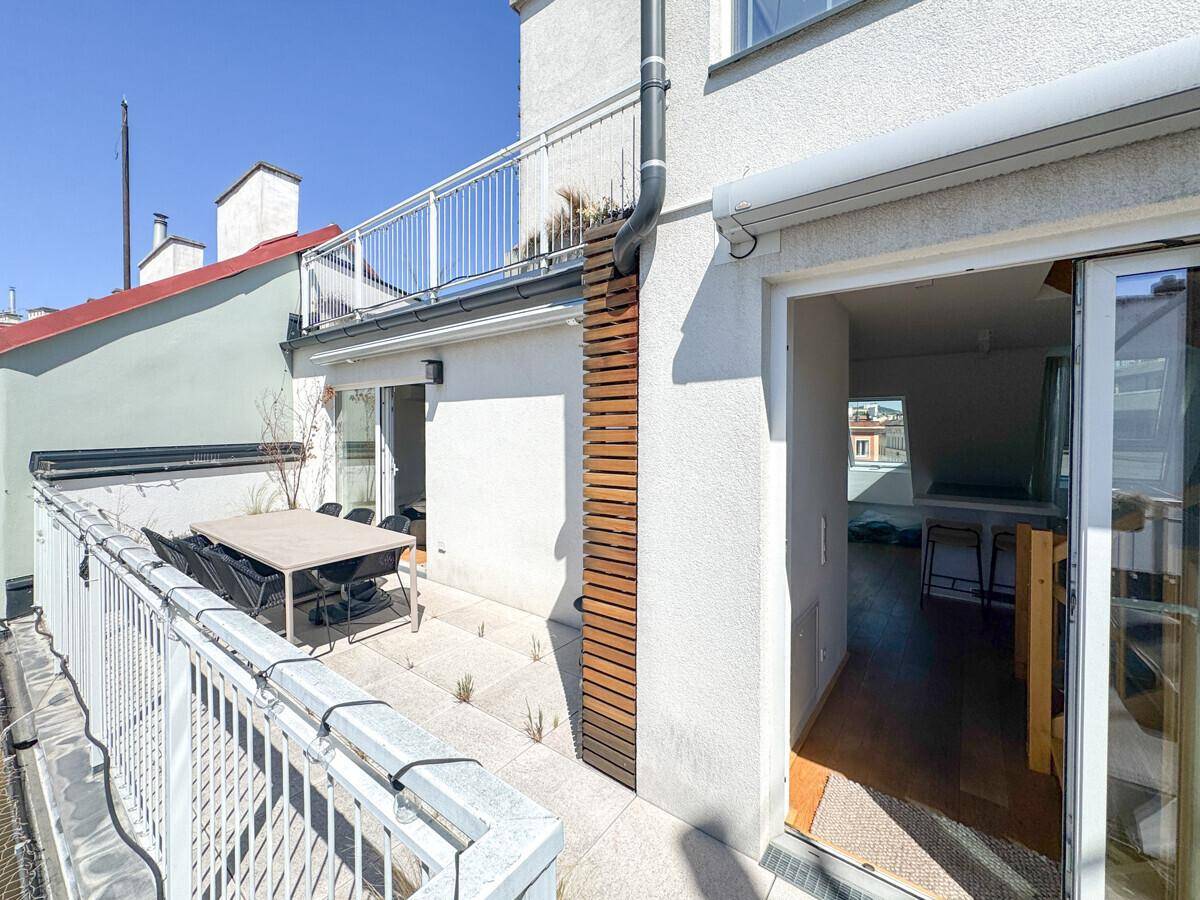 Gemütliche Terrasse mit Essbereich und direktem Zugang zu einem hellen Innenraum.