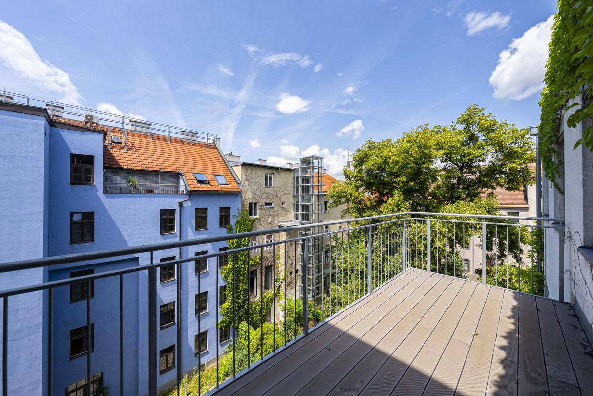 Balkon mit Holzboden und Metallgeländer, bietet einen grünen Blick auf die umliegenden Gebäude.