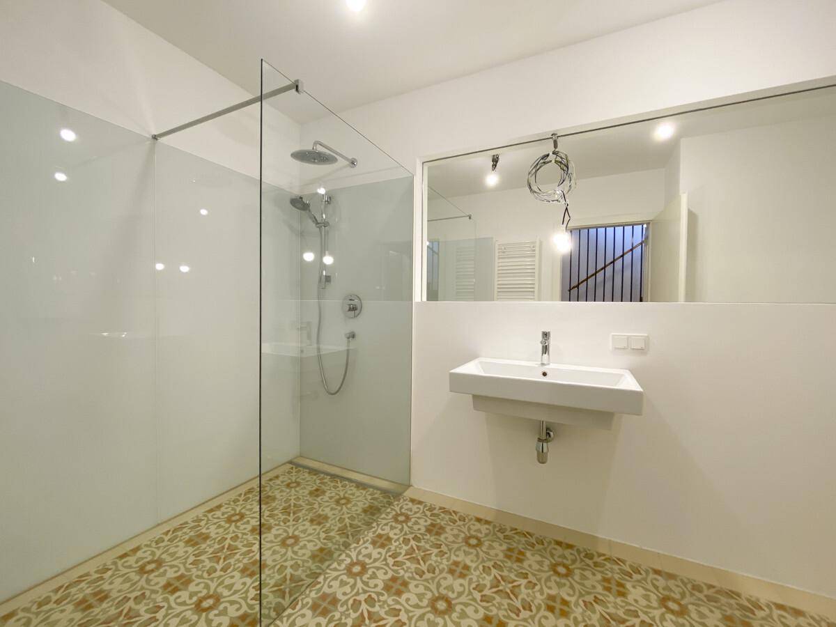 Modernes Badezimmer mit begehbarer Dusche, großem Spiegel und gemusterten Bodenfliesen.