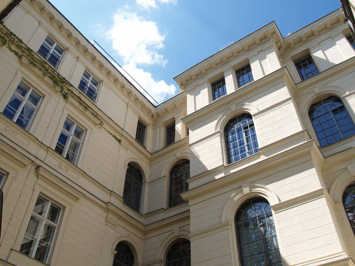 Blick auf die helle Fassade eines Gebäudes mit klassischen architektonischen Details und Bogenfenstern.