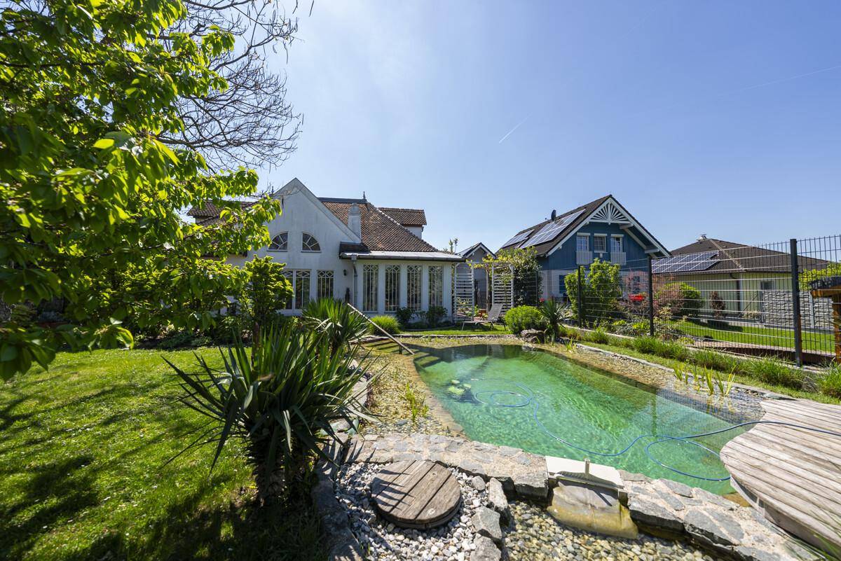Gartenansicht des Hauses mit Schwimmteich, umgeben von üppigem Grün und Nachbarhäusern im Hintergrund.