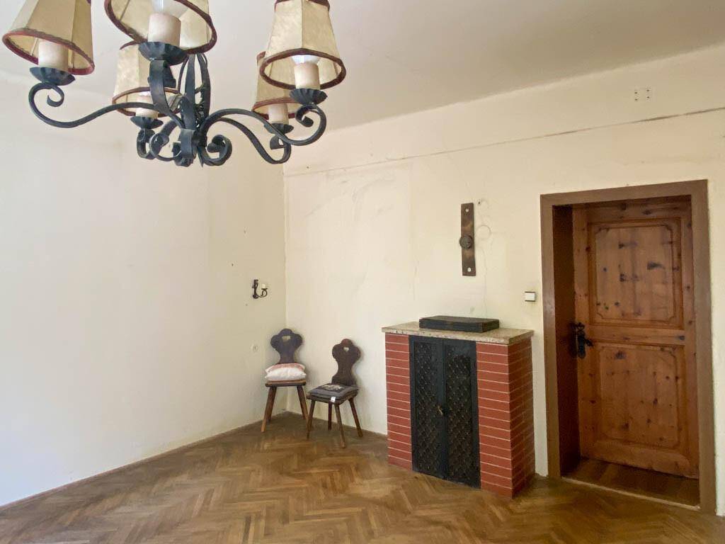 Geräumiges Zimmer mit Fischgrätparkett, einem traditionellen Kachelofen und einem antiken Kronleuchter.