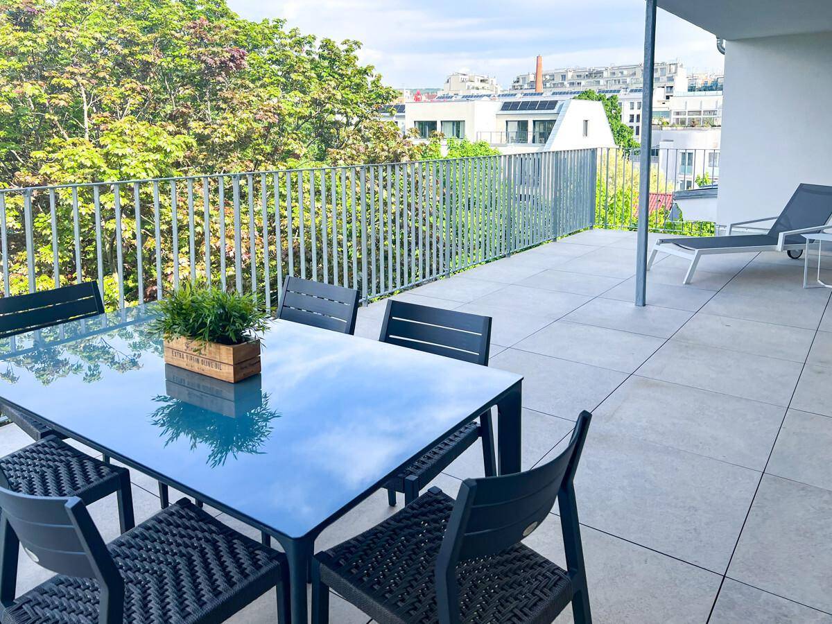 Geräumige Dachterrasse mit Esstisch und Liegestuhl, umgeben von viel Grün und Stadtblick.