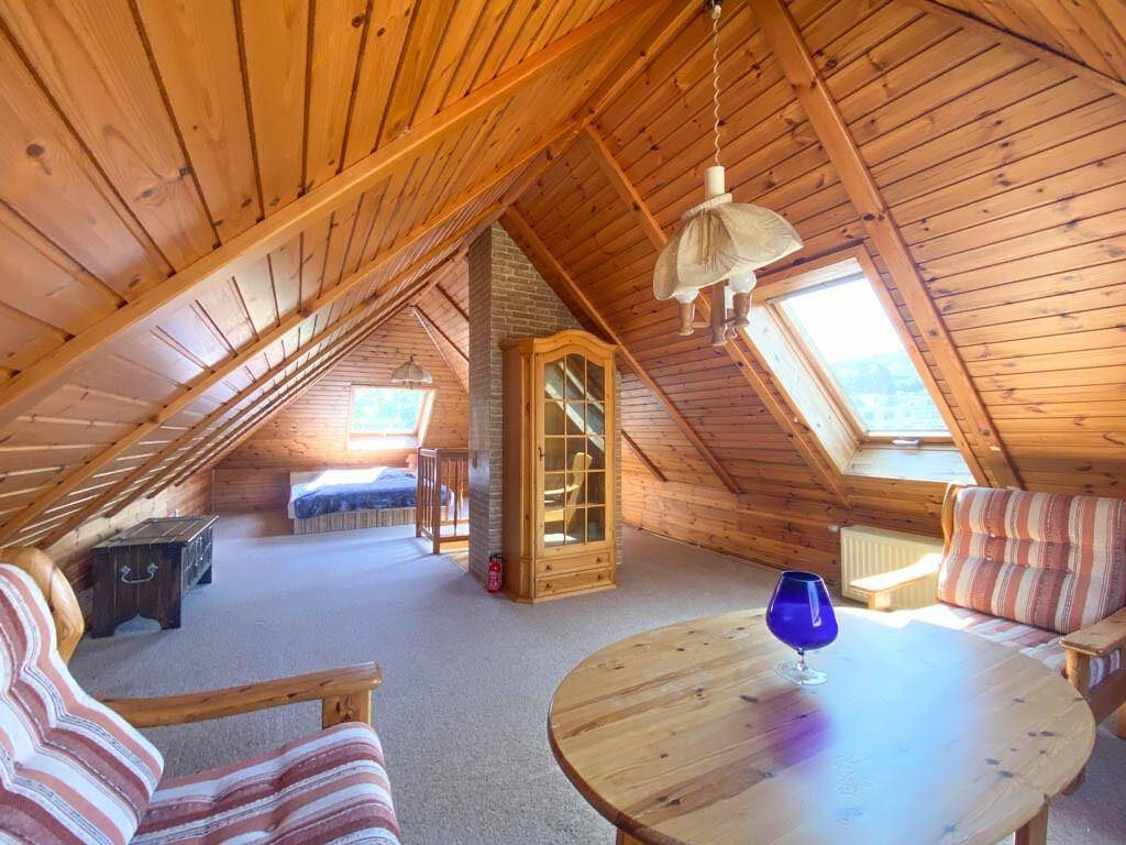 Geräumiger Dachboden-Wohnbereich mit Holzverkleidung, Dachfenstern und rustikalen Sitzmöbeln.