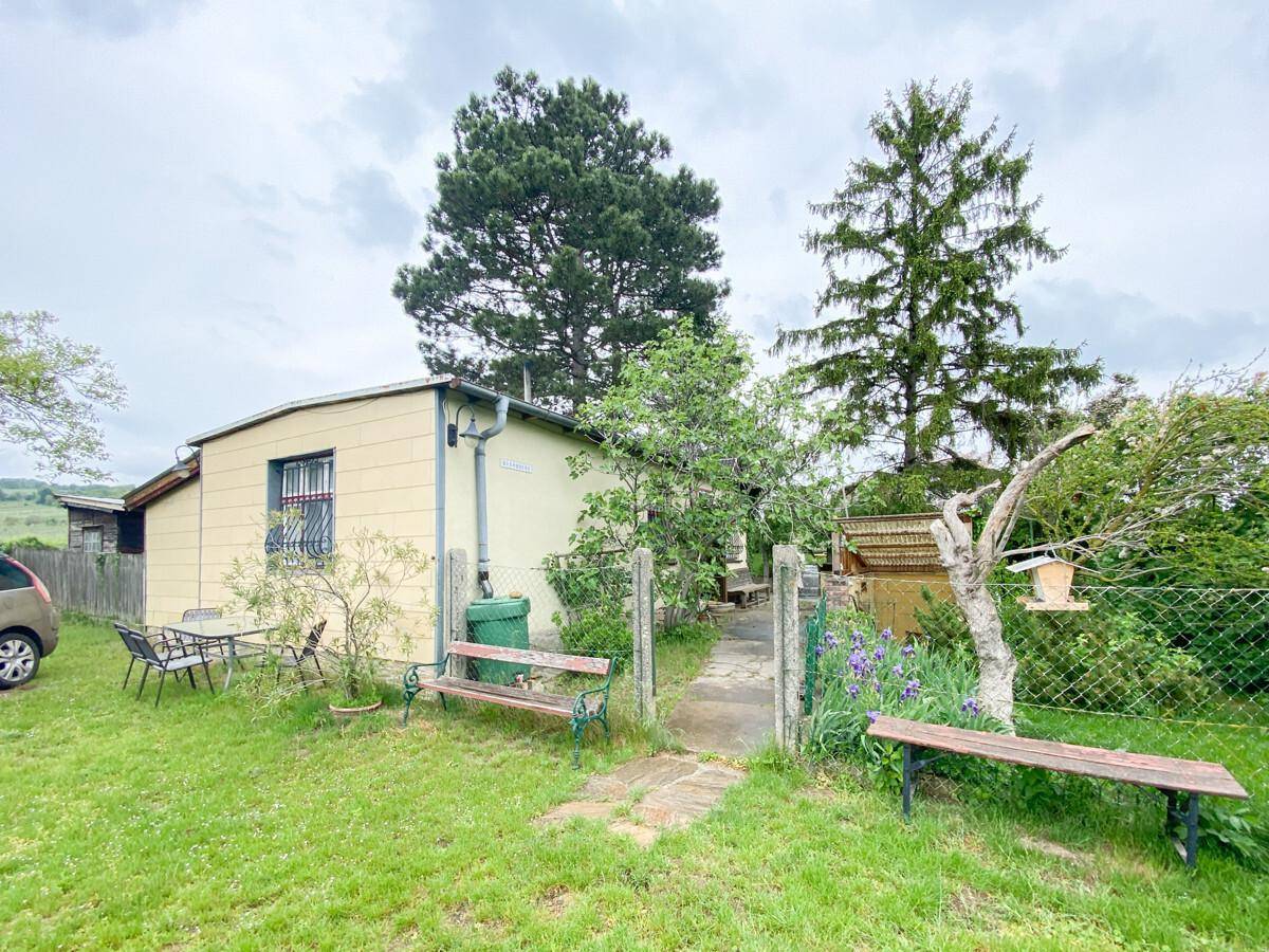 Außenansicht eines kleinen Hauses mit Garten, Sitzbänken und viel Grünfläche.