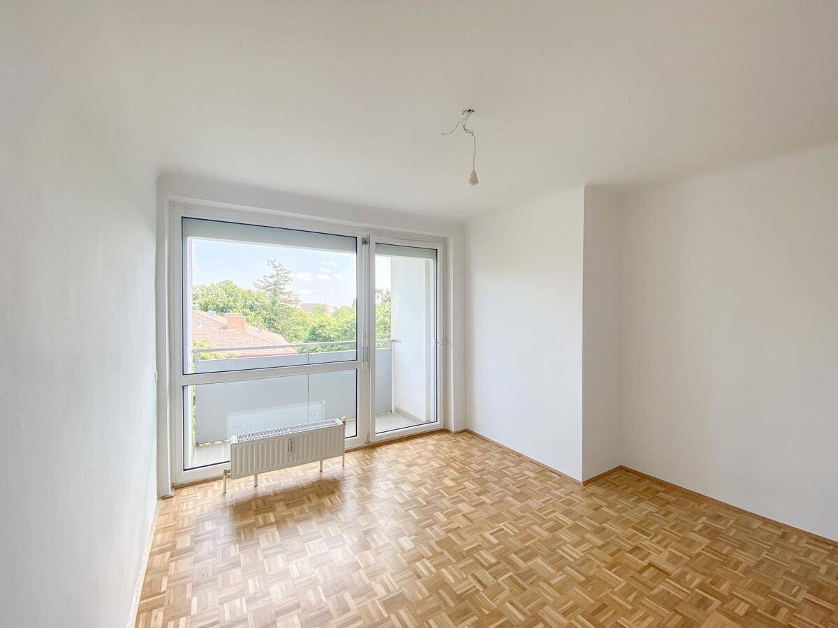 Schlafzimmer mit Parkettboden, großem Fenster und Zugang zu einem kleinen Balkon.
