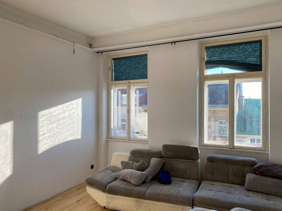 Helles Wohnzimmer mit großem Sofa und zwei Fenstern, durch die Sonnenlicht fällt.