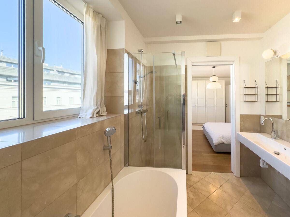Modernes Badezimmer mit Badewanne, Glasdusche und Fenster für natürliches Tageslicht.
