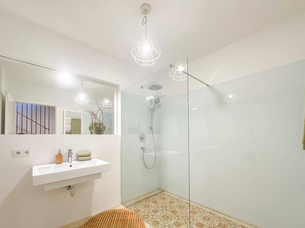 Helles Badezimmer mit großer begehbarer Dusche, modernem Waschbecken und Spiegel.