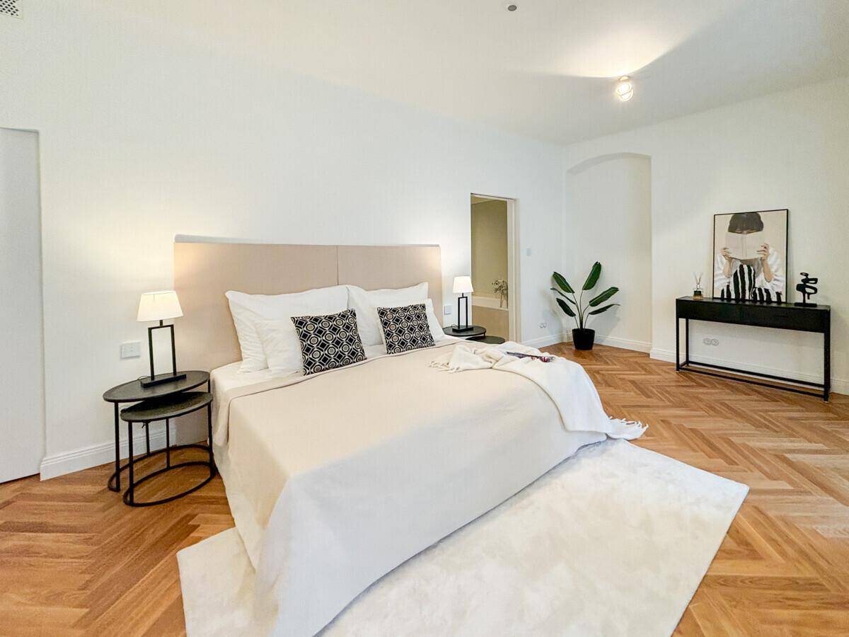 Geräumiges Schlafzimmer mit hellem Bett, modernen Nachttischen und Fischgrätparkett.