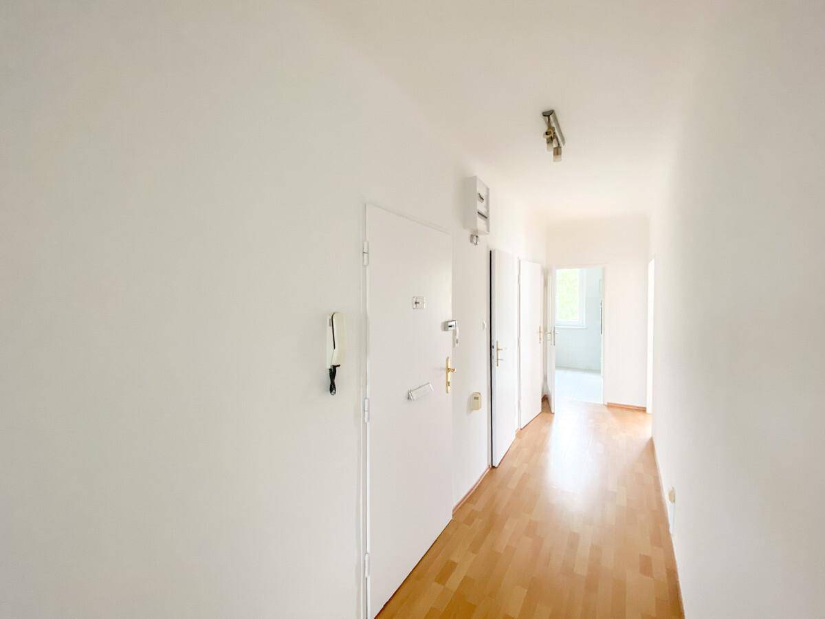 Langer, heller Flur mit Holzboden und mehreren Türen, der den Eingangsbereich verbindet.