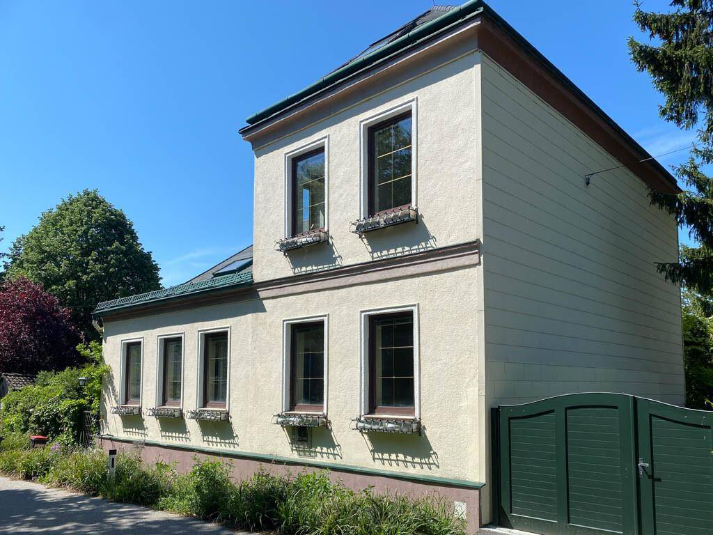 Attraktive Hausfassade mit mehreren Fenstern und einem grünen Tor unter blauem Himmel.