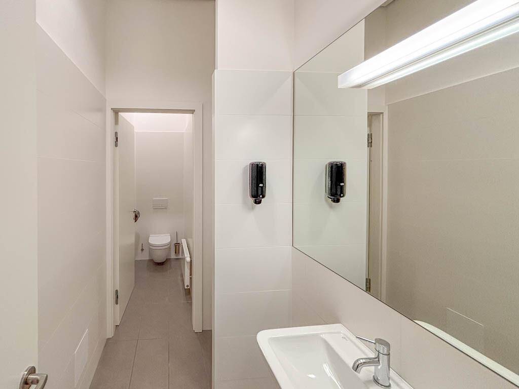 Modernes Badezimmer mit weißen Fliesen, großem Spiegel, Waschbecken und Seifenspendern.