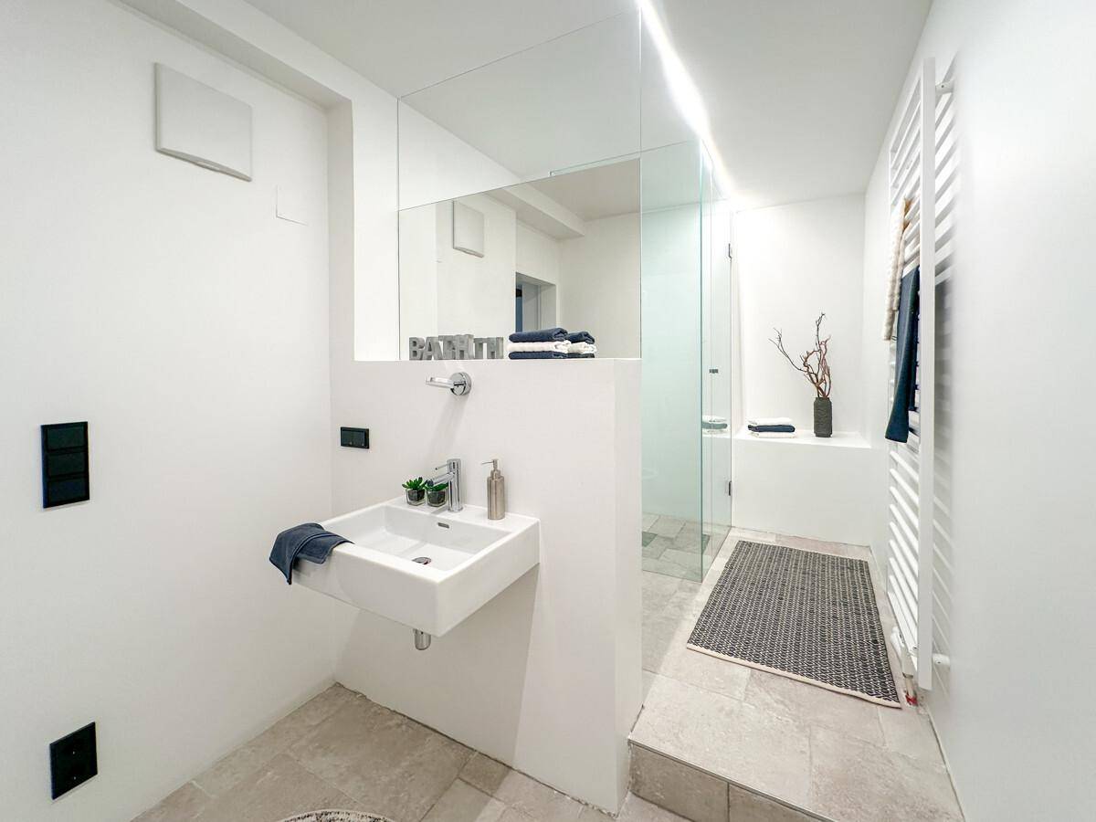 Modernes Badezimmer in Weiß mit ebenerdiger Dusche, Einzelwaschbecken und beheiztem Handtuchhalter.