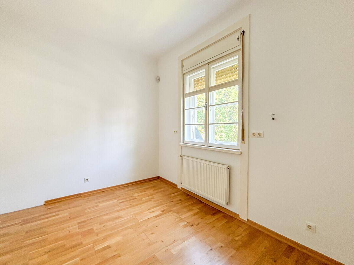 Helles Schlafzimmer mit Holzboden und großem Fenster mit Blick ins Grüne.