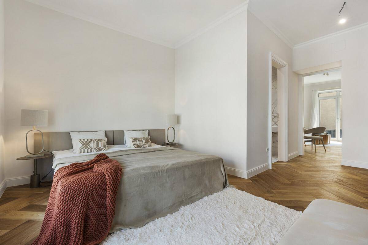 Helles Schlafzimmer mit Fischgrätparkett, hohen Decken und Blick in den angrenzenden Wohnbereich.