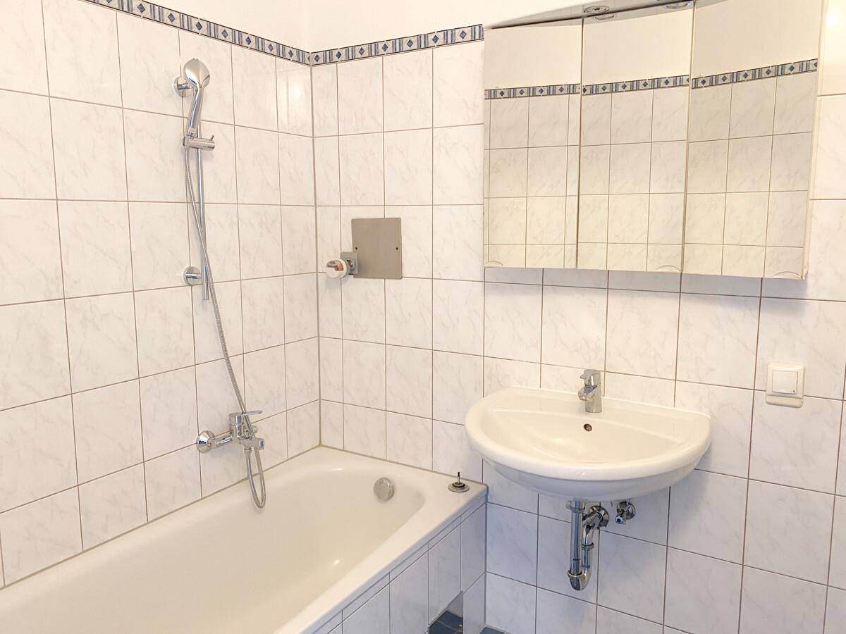 Badezimmer mit Badewanne, Waschbecken und weißen Fliesen in gutem Zustand.