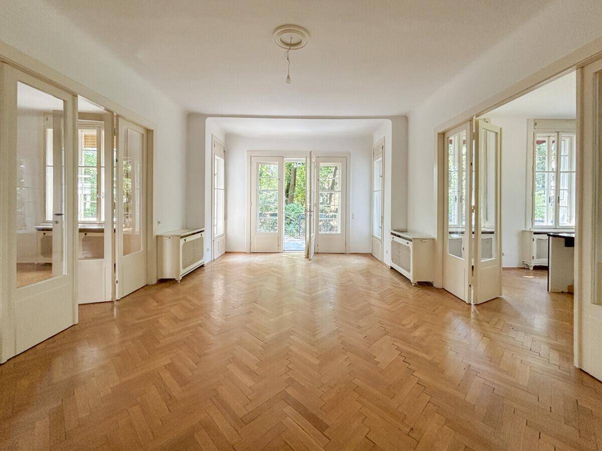 Geräumiges Wohnzimmer mit Fischgrätparkett, hohen Decken und großen Flügeltüren zum Garten.