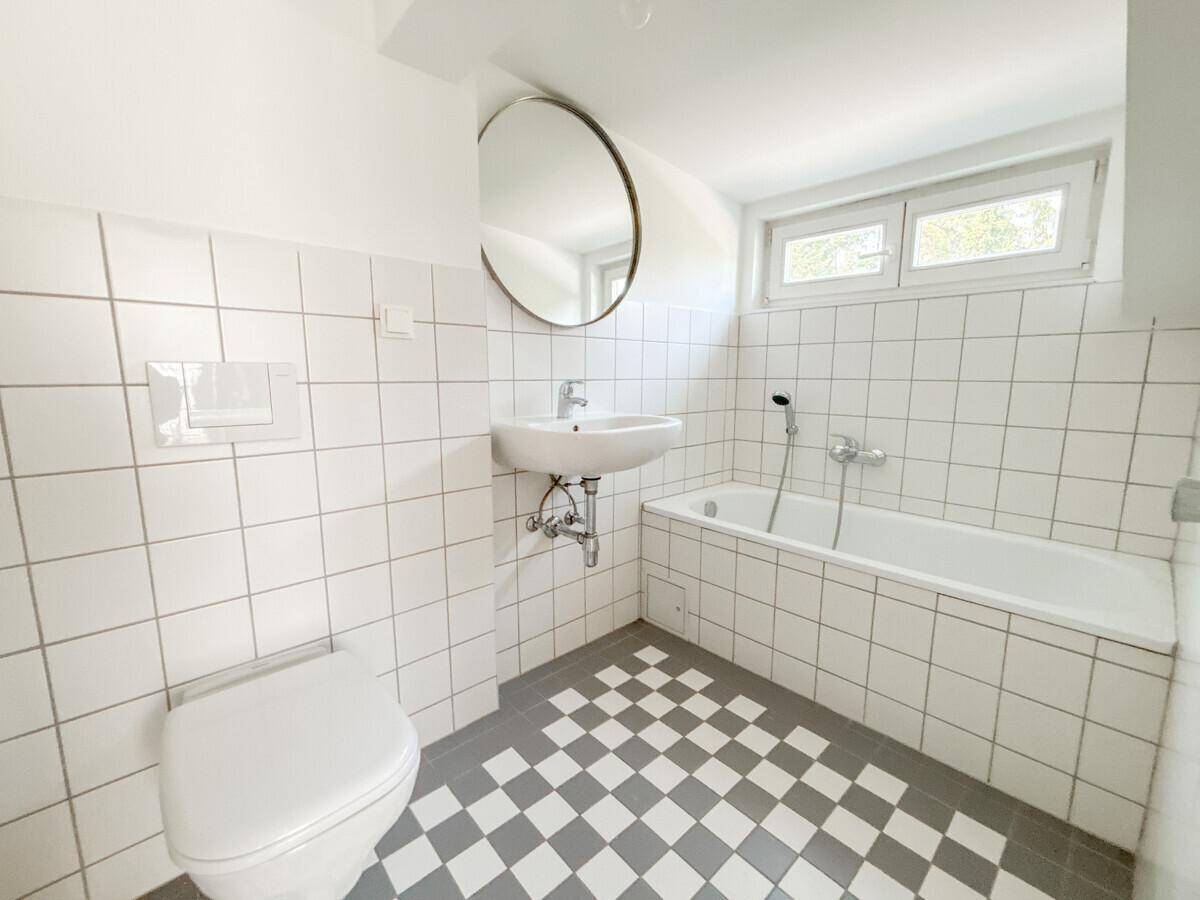Helles Badezimmer mit Badewanne, WC, Waschbecken und schwarz-weißem Schachbrettmuster-Fliesenboden.