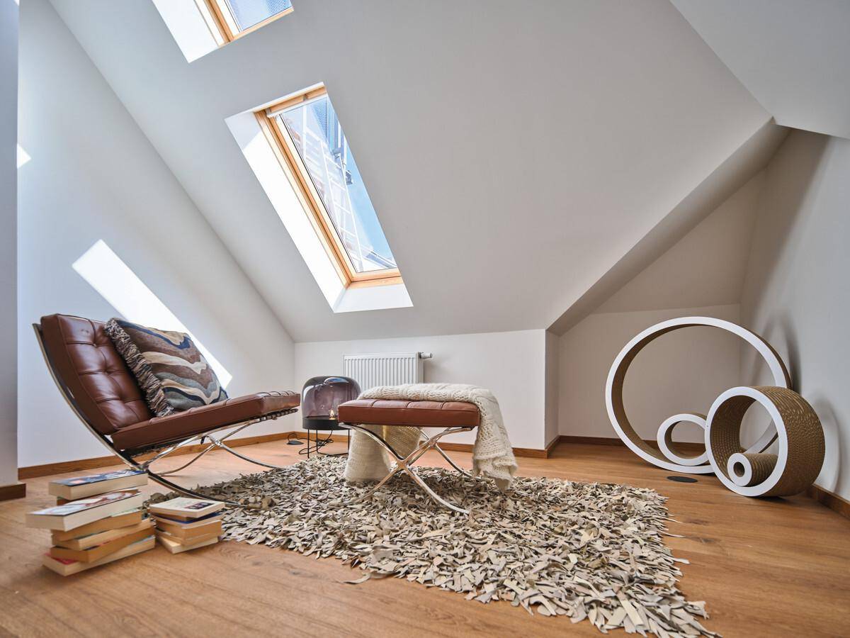 Gemütlicher Dachbodenraum mit Holzboden, schrägen Wänden und mehreren Dachfenstern für viel Tageslicht.