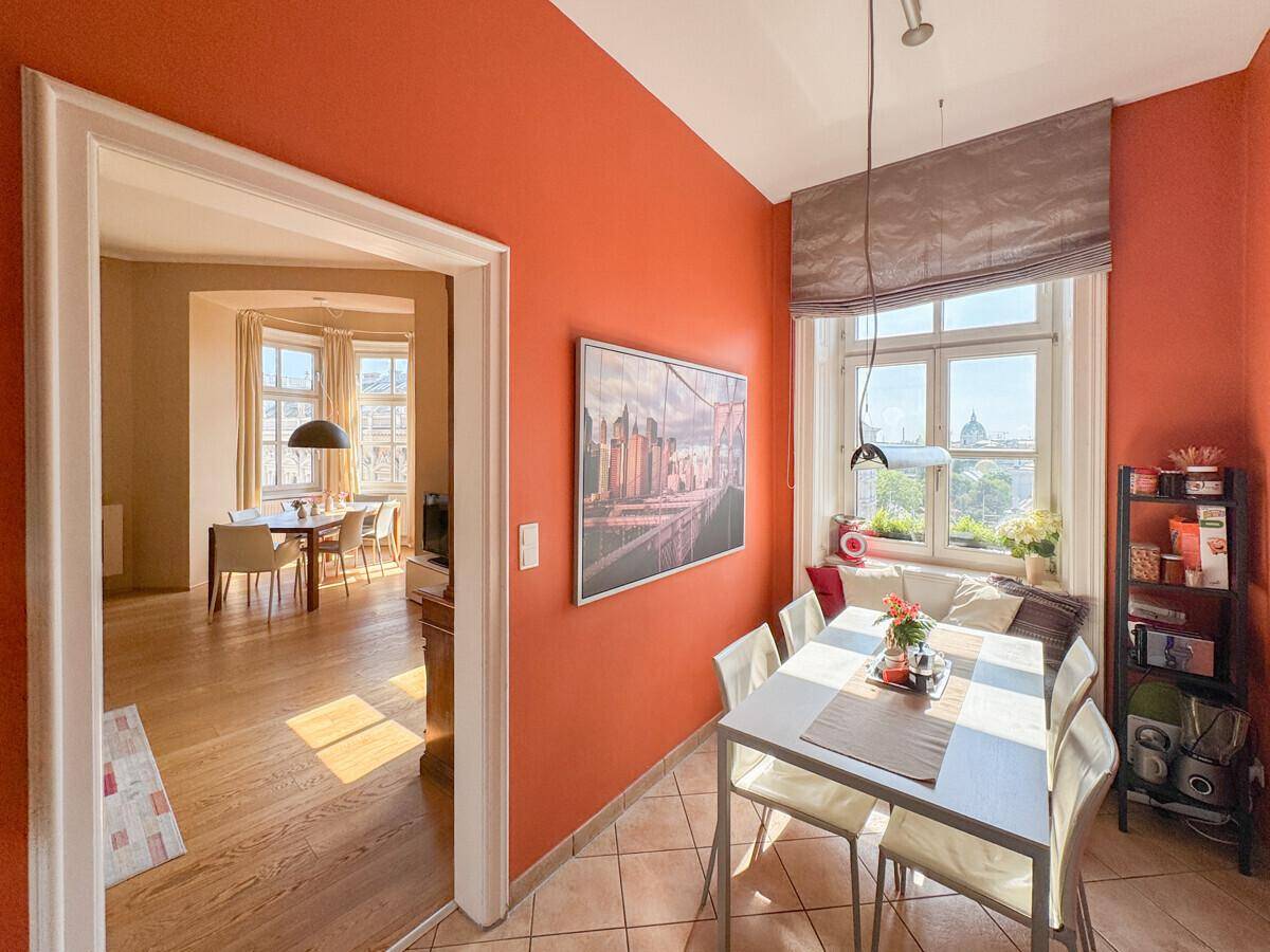 Essbereich in der Küche mit orangefarbenen Wänden, Fliesenboden und Fensterblick.