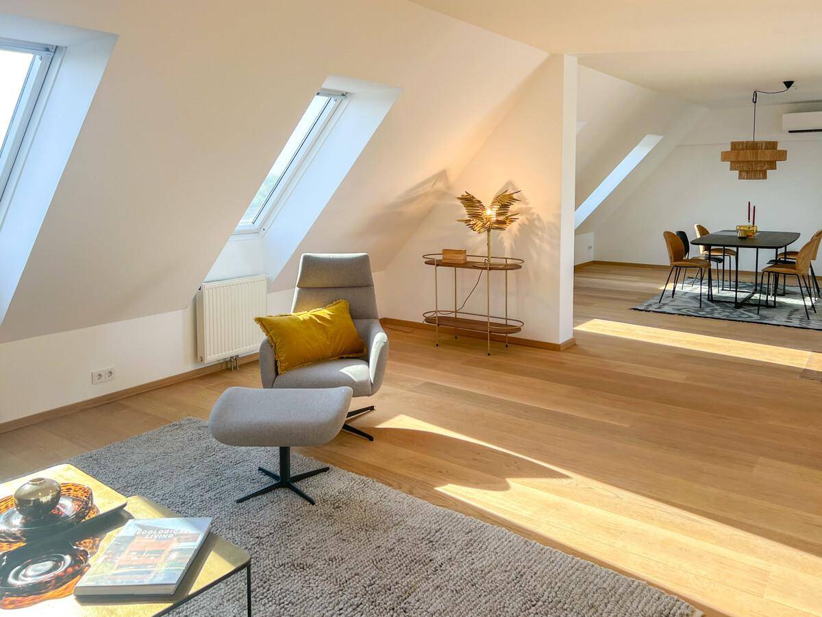 Helles Dachgeschoss-Wohnzimmer mit Holzboden, gemütlichem Sessel und Blick auf den Essbereich.