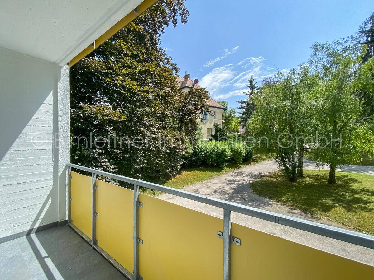 Balkon mit gelbem Geländer und Blick auf die grüne Umgebung und das historische Gebäude.