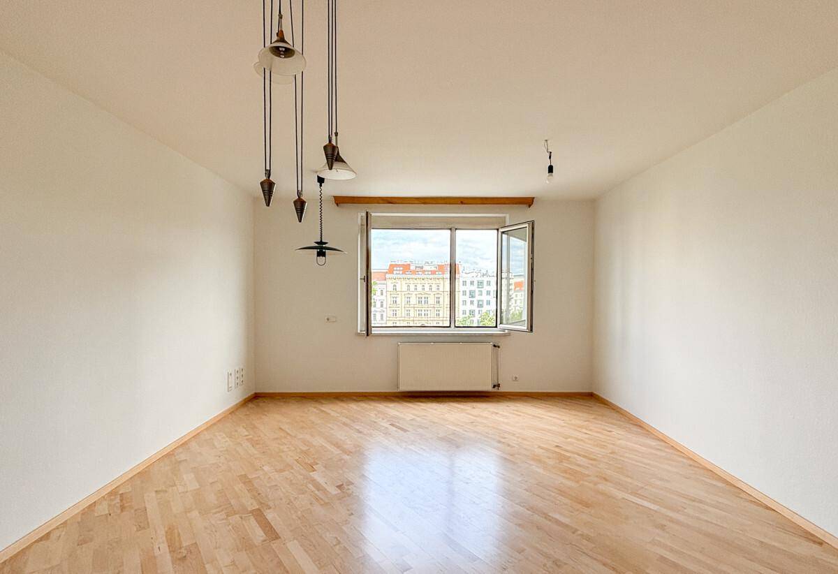 Geräumiges, leeres Zimmer mit Parkettboden und Blick auf die Stadt durch das Fenster.