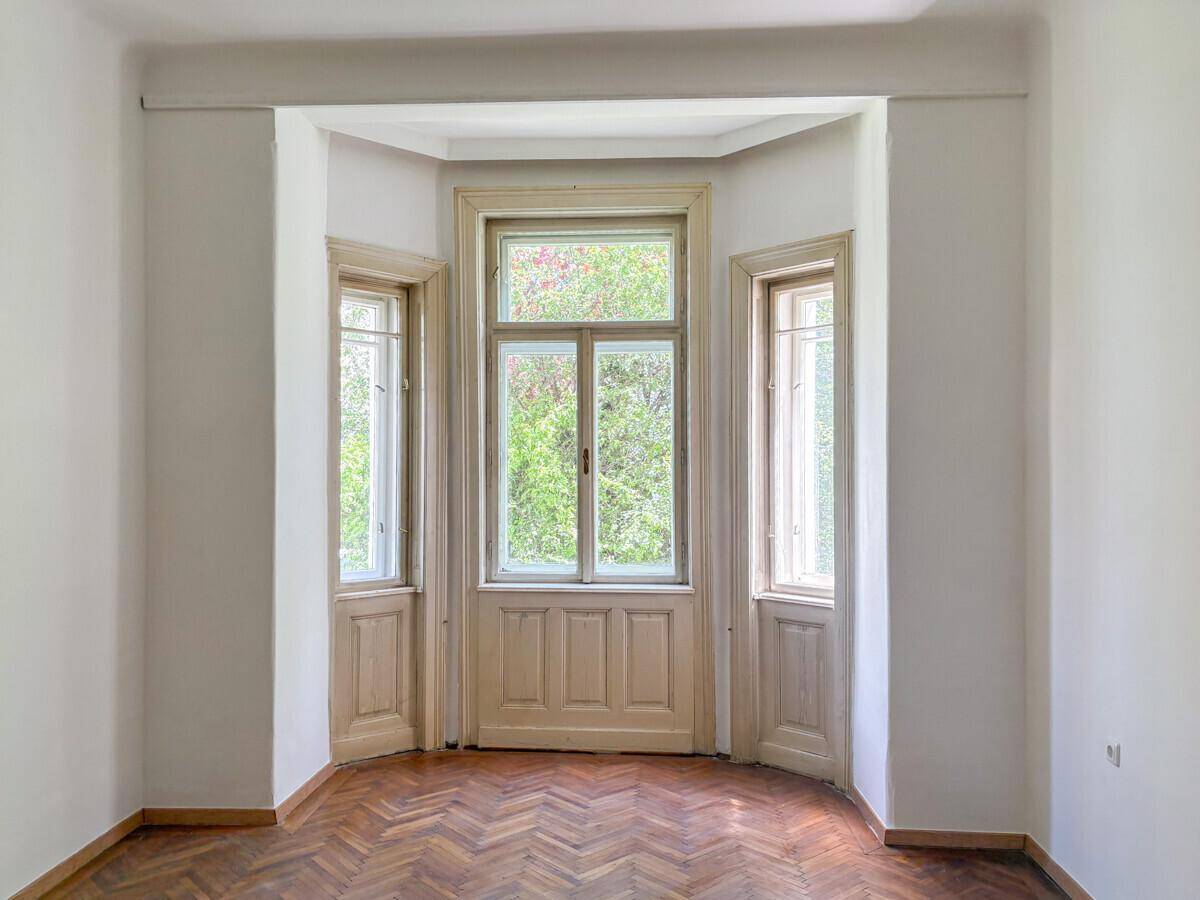 Heller Raum mit Erkerfenstern und klassischem Fischgrätparkettboden, umgeben von viel Grün.