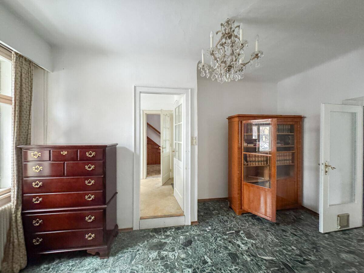 Zimmer mit dunklem Marmorboden, einem eleganten Kronleuchter und antiken Holzmöbeln.