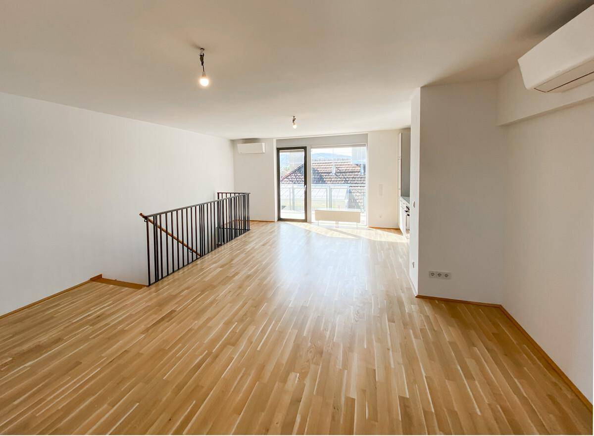 Geräumiger Wohnbereich mit Holzparkett, Treppe zum Obergeschoss und Zugang zu einem Balkon.