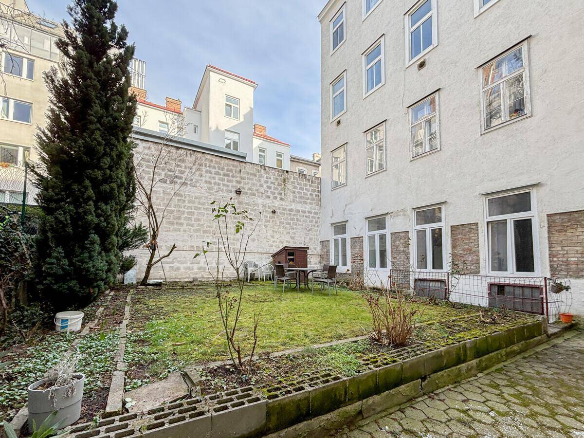 Kleiner Hinterhofgarten mit Rasenfläche und Sitzgelegenheiten, umgeben von hohen Mauern.