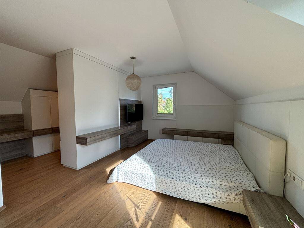 Schlafzimmer mit Doppelbett, integrierten Möbeln und Holzboden unter schräger Decke.