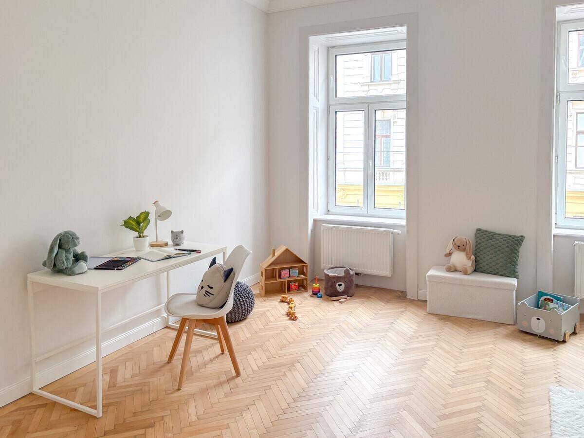 Kinderzimmer mit Schreibtisch, Spielzeug und Fischgrätparkett, ideal zum Lernen und Spielen.