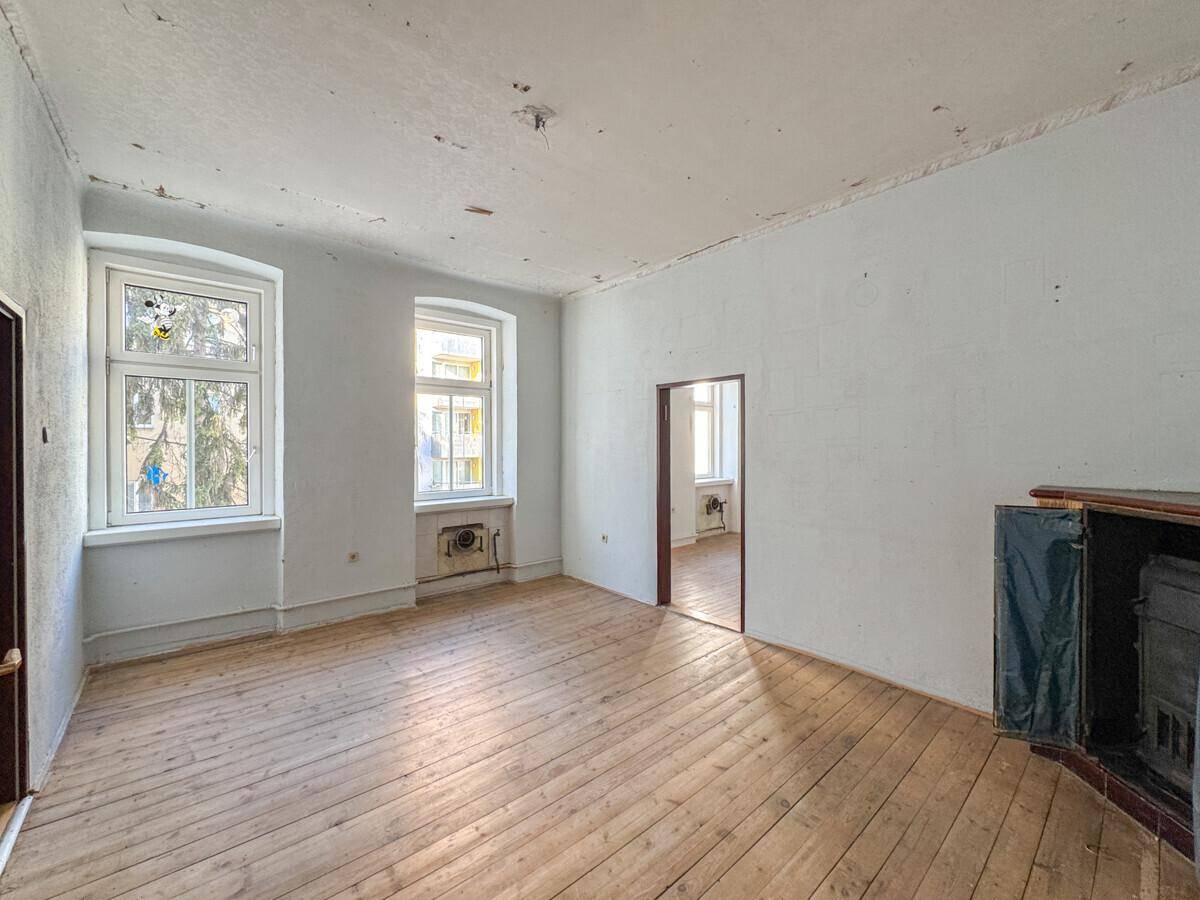 Leeres Zimmer mit Dielenboden und einem alten Ofen, der auf eine Modernisierung wartet.