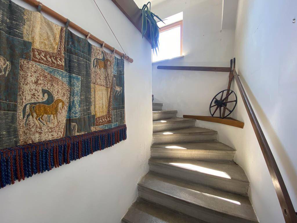Geschwungene Steintreppe mit Holzgeländer und einem dekorativen Wandteppich.
