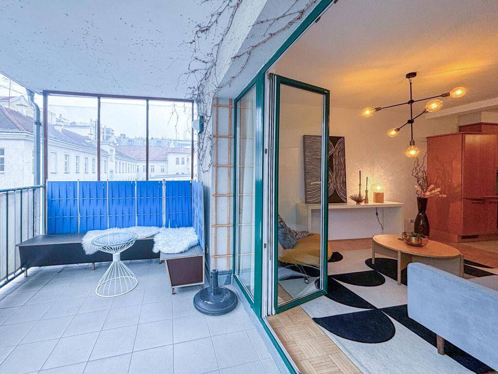 Gemütlicher Balkon mit Sitzgelegenheiten, Fliesenboden und Blick auf die umliegenden Gebäude.