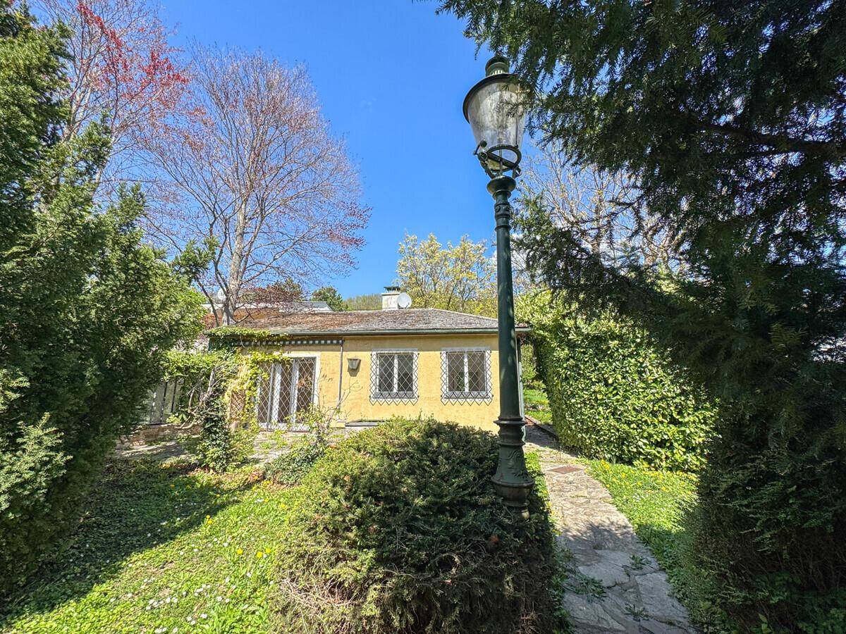 Gartenweg führt zum Haus, umgeben von hohen Hecken und Bäumen, mit einer klassischen Laterne.
