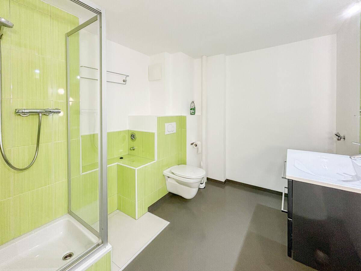 Modernes Badezimmer mit grünen Fliesen, Duschkabine und wandhängendem WC.