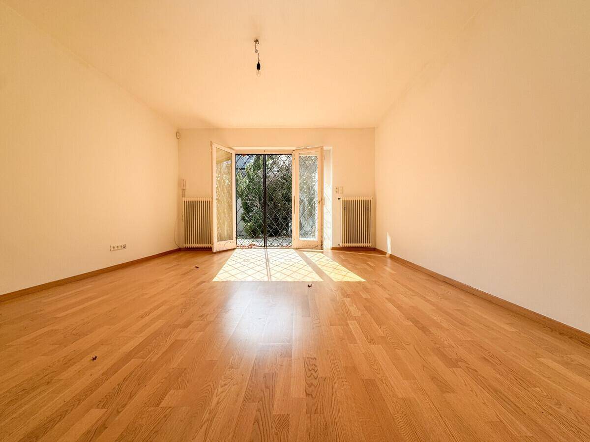 Heller Wohnbereich mit Parkettboden und großen Fenstertüren, die viel Sonnenlicht hereinlassen.
