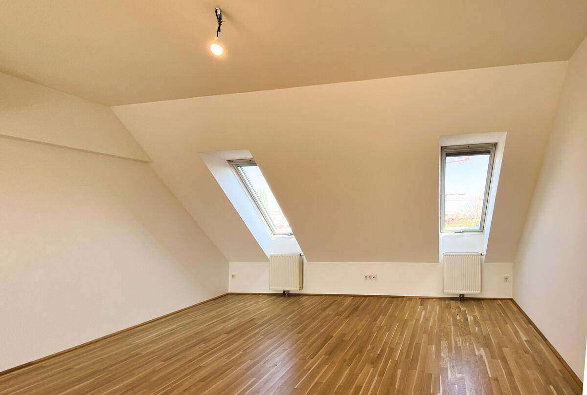 Helles Schlafzimmer im Dachgeschoss mit schrägen Wänden, Parkettboden und Dachfenstern.